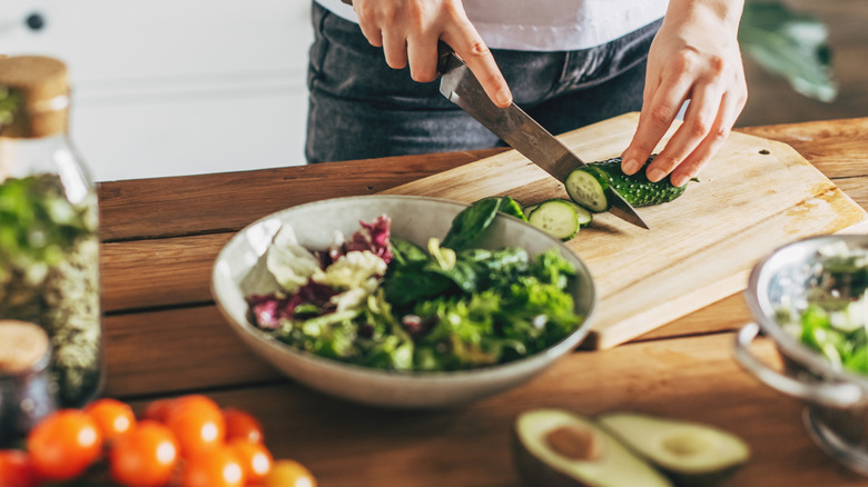 woman hands making salad on table with fresh colorful vegetables