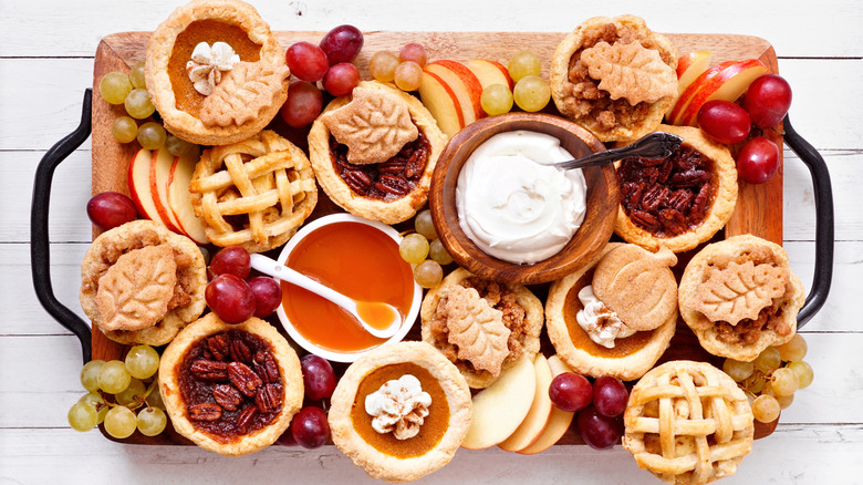 fall dessert tray with mini pies, a dish of whipped cream, and apple slices and grapes