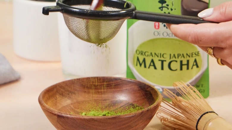 Hand sifting matcha into bowl with whisk and product package on table