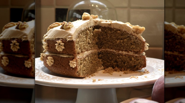 Mirrored image, coffee and walnut cake with slice removed on white cake stand in kitchen