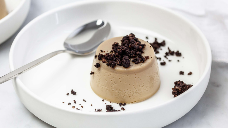 Coffee panna cotta with cocoa almond crumble on white plate with spoon