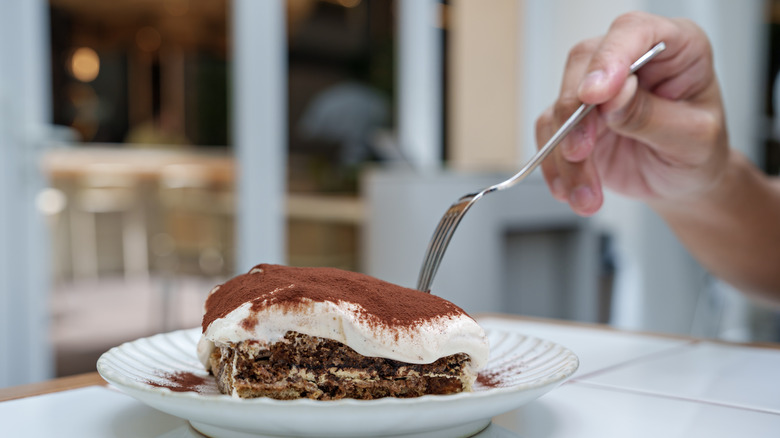 close up of person holding fork to plate with tiramisu