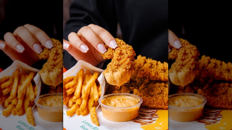Hand dipping Popeyes Spicy Chicken Tender in sauce