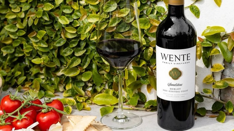 A bottle and glass of Wente Sandstone merlot with crackers, tomatoes and cheese
