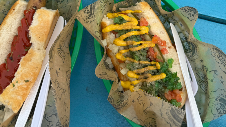 Two hot dogs sitting in wrappings in green baskets on a blue table