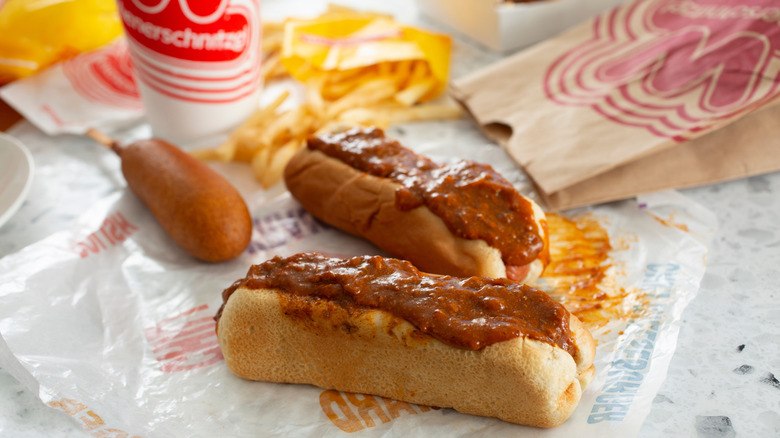 Two chili dogs sitting near a corn dog and some spilt fries