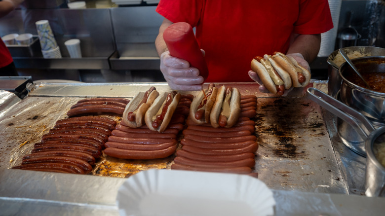 A cook preparing many hot dogs on a large griddle