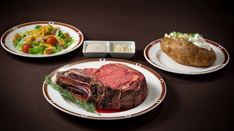 Prime rib on plate with other plates of salad and baked potato