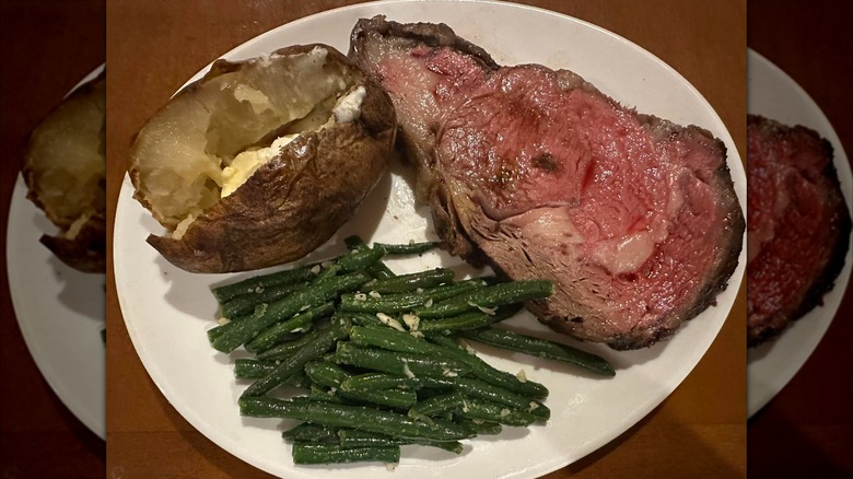 Slice of prime rib with green beans and baked potato
