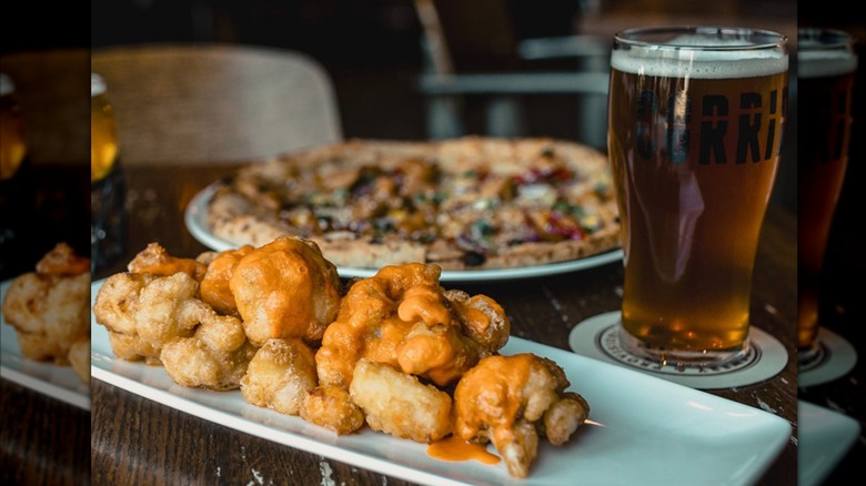 the cauliflower and curds, a pizza, and a beer from corridor brewery all on a table