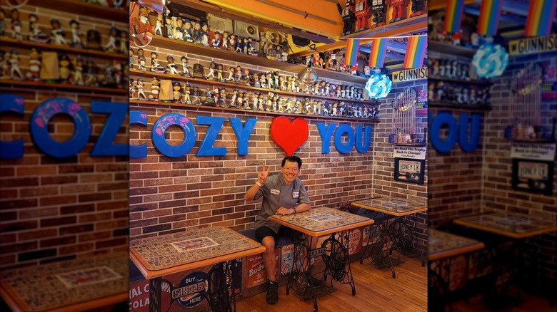 Chef Tee of Cozy Noodles and Rice posing at one of the tables in his restaurant with the elaborate decor visible