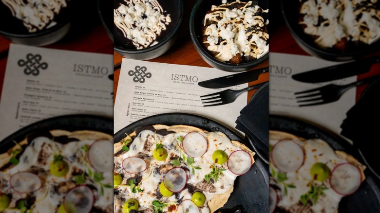 A stunning plate of food with two side dishes resting on top of a printed menu for Istmo Oaxacan Cuisine