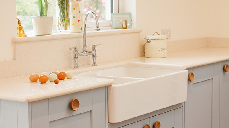 Close up of kitchen with farmhouse sink, eggs on white countertop and pale blue cabinets