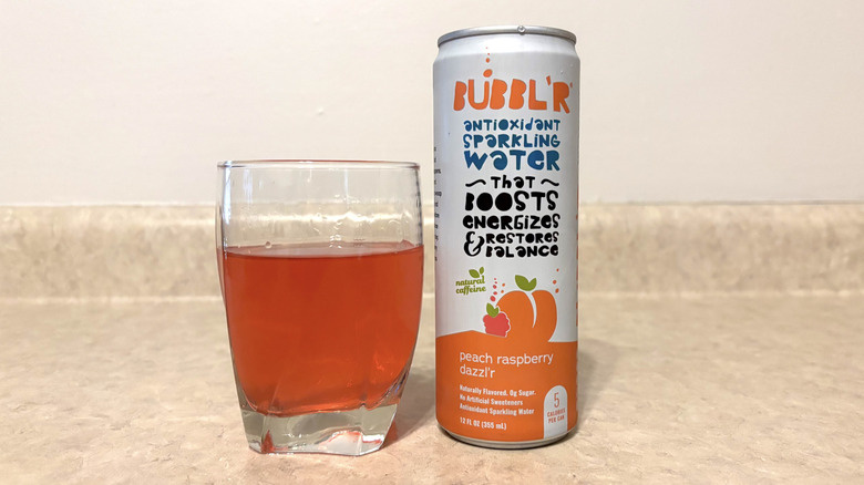 Bubbl'r Peach Raspberry Dazzl'r in can and glass on neutral background.