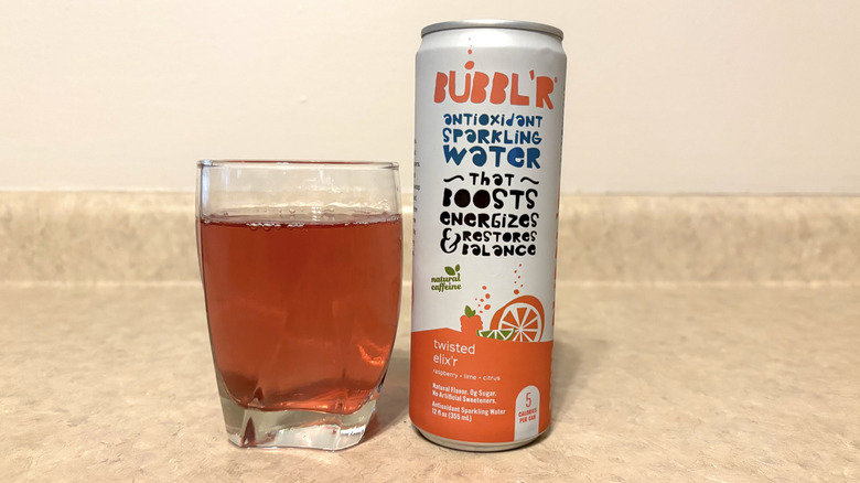 Bubbl'r Twisted Elix'r in can and glass on neutral background.