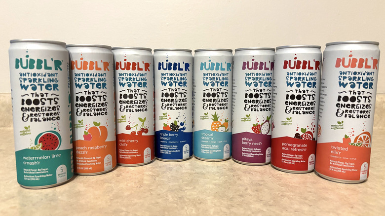 An assortment of Bubbl'r sparkling water cans on a neutral background.