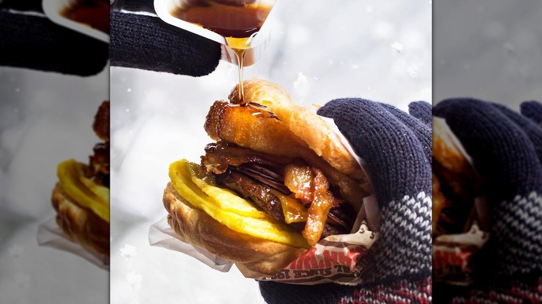 Gloved hand pouring maple syrup onto Burger King Croissan'wich, that's been stuffed with French toast sticks