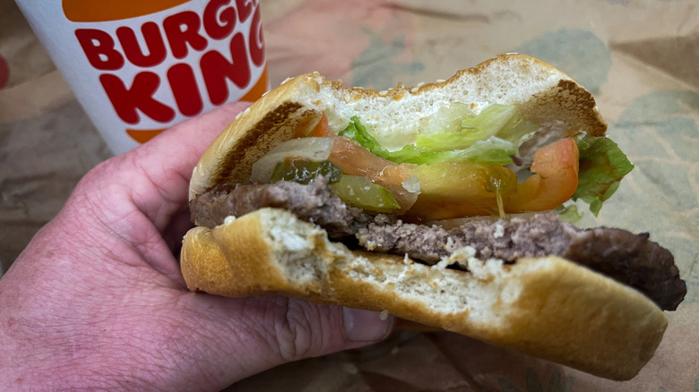 hand holding a half eaten Whopper burger in front of Burger King drink