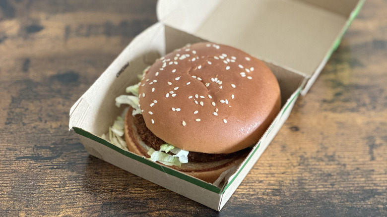 Cardboard box with burger with sesame seed bun visible on wooden table