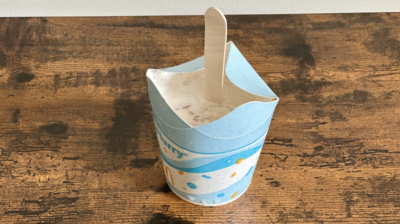 Small cardboard cup with ice cream and wooden spoon on wooden table