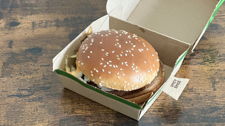 Cardboard box with burger with sesame seed bun visible on wooden table