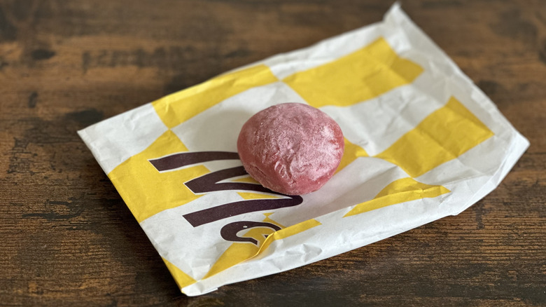 White and yellow bag with small pink powdered donut on wooden table