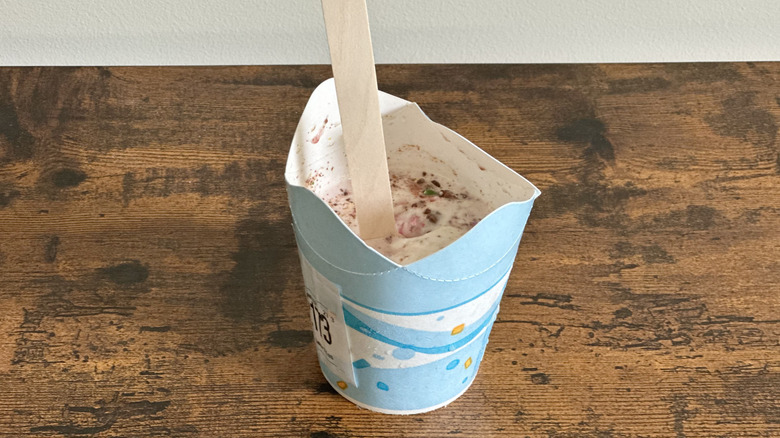 Small cardboard cup with ice cream and wooden spoon on wooden table