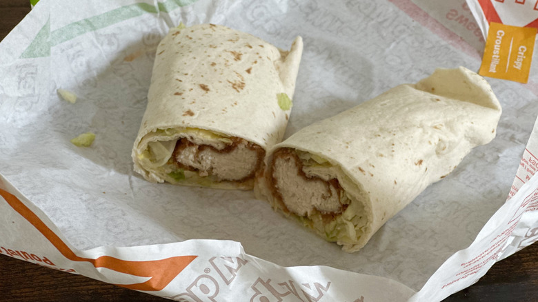 Paper wrapper with wrap cut in half with visible fried chicken and lettuce