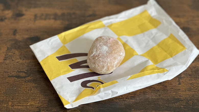 White and yellow bag with white powdered donut on wooden table