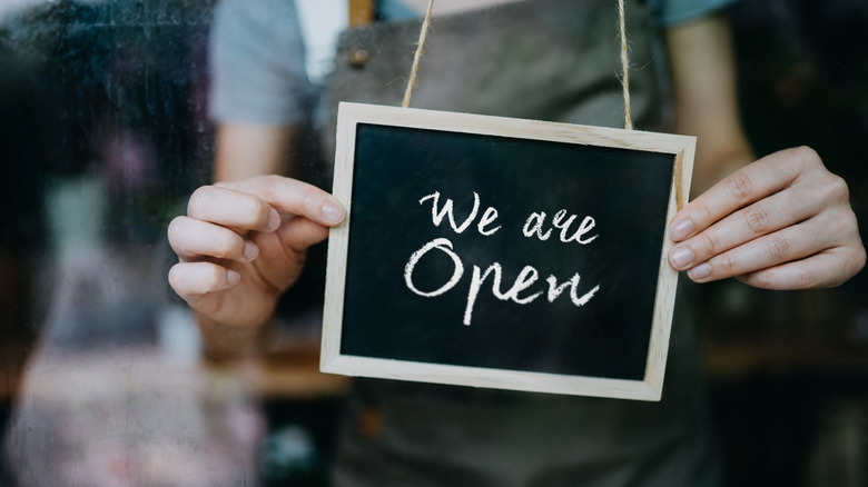 cafe owner hanging an "open" sign on the door of the business