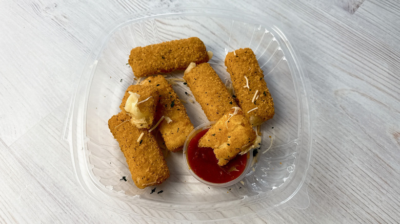 TGI Fridays fried mozzarella in a takeout container with a side of marinara sauce