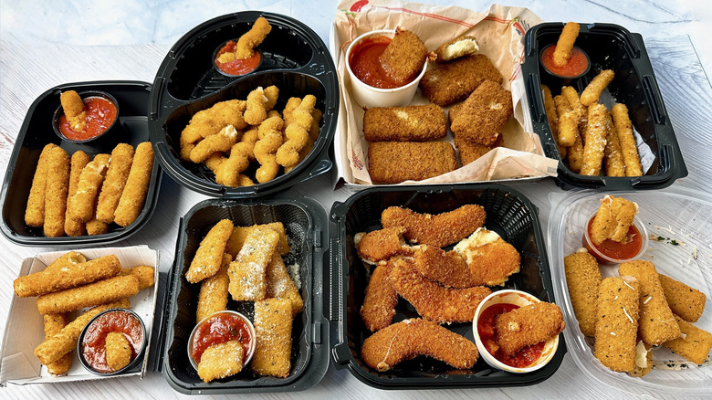 8 restaurant mozzarella sticks in takeout containers with marinara dipping sauce alongside