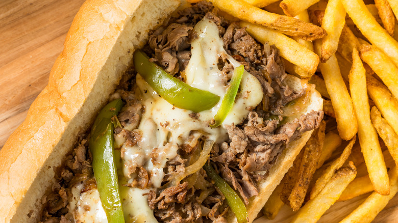 Philly cheesesteak close-up with peppers and fries in the background