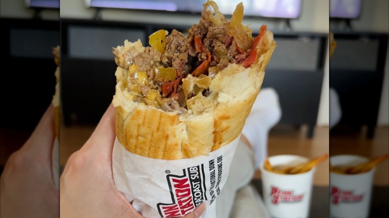 Half-eaten Philly cheesesteak held in front of blurred television