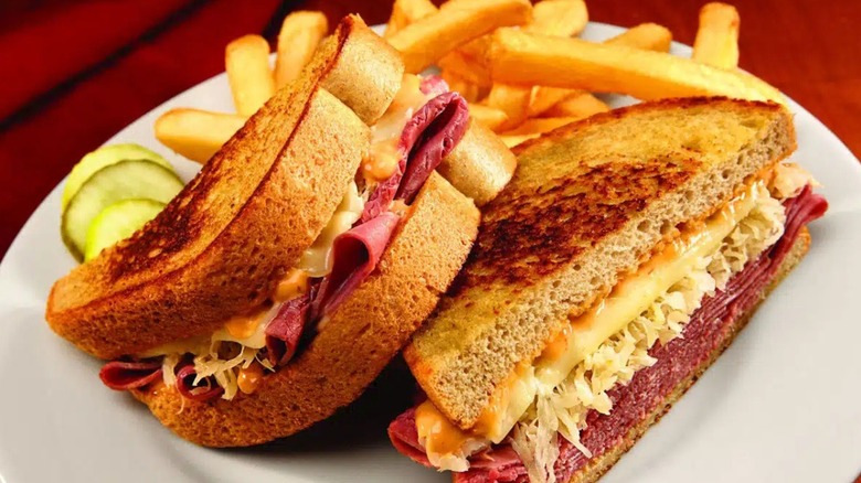 A Reuben sandwich, fries, and pickle slices sitting on a plate
