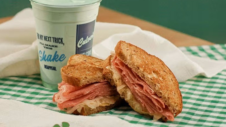 A sliced sandwich and a green shake sitting on a checkerboard tablecloth