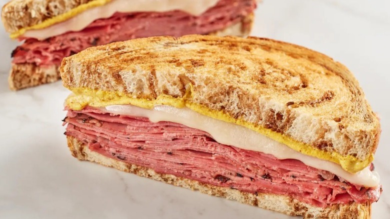 A close up of half of a sandwich with the other half sitting off in the background