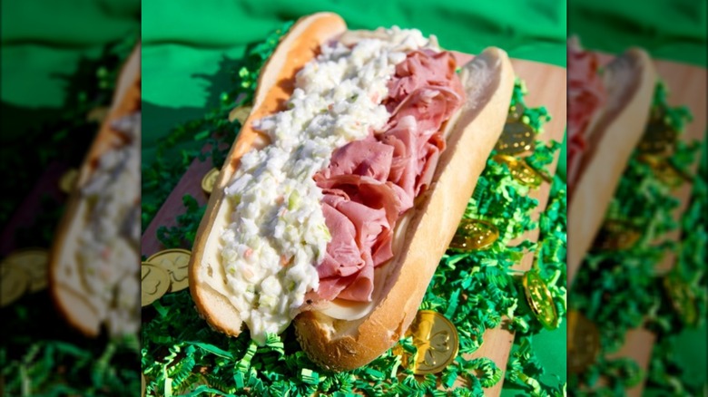 A sub sandwich with corned beef and coleslaw sitting on green confetti