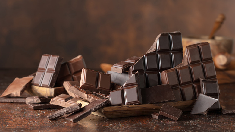 A pile of broken milk and dark chocolate bar pieces on a brown background