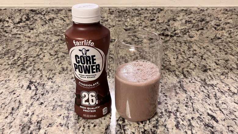 A bottle of Fairlife Core Power Chocolate 26G Protein Shake sits next to a clear glass containing the shake