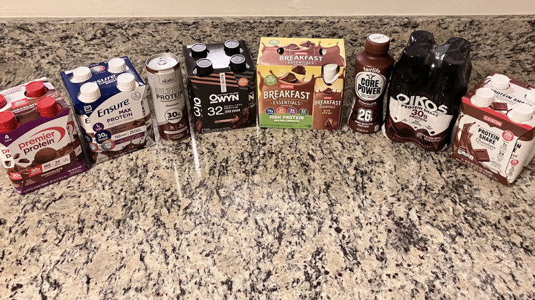 Eight chocolate protein shakes sit next to each other in a semi-circle on a counter