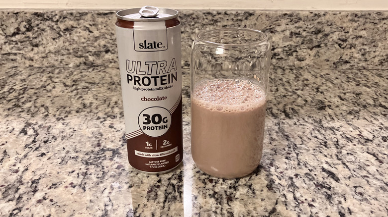 A can of Slate Milk Chocolate Ultra 30g Protein Shake sits next to a clear glass containing the shake