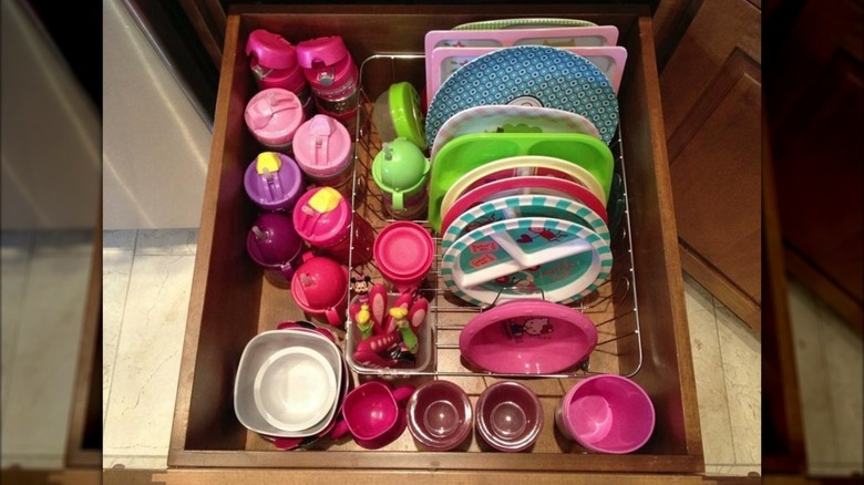A dish rack in a drawer holding kids dishes and cups