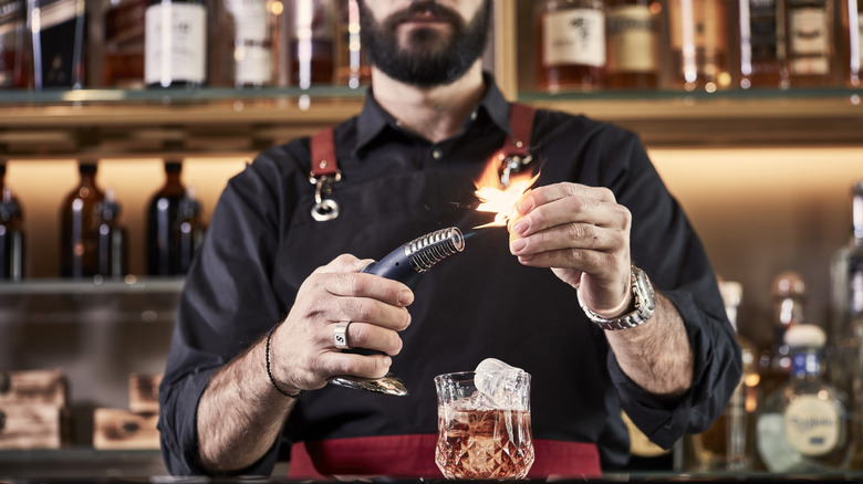 a bartender torching a garnish for a cocktail