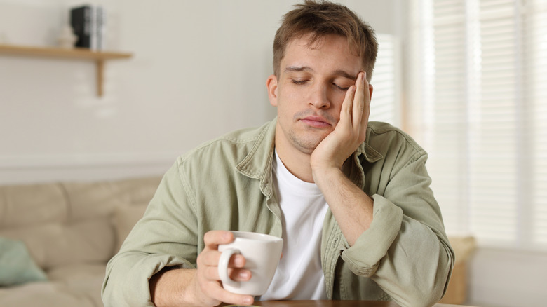 Unhappy young man with cup of coffee sitting at wooden table