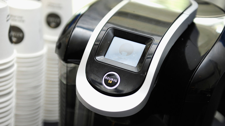 A Keurig coffee maker next to stacks of cups