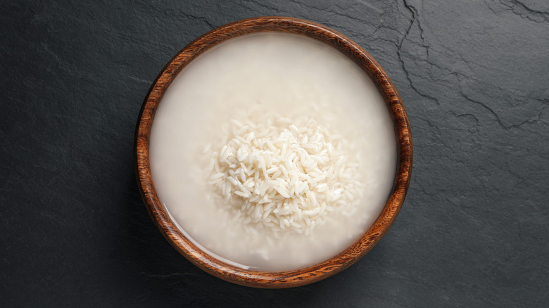 Water and rice in wooden bowl on black countertop