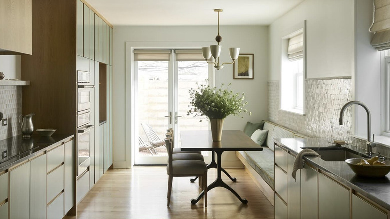 A sage green kitchen with a booth and table seating area at the far end