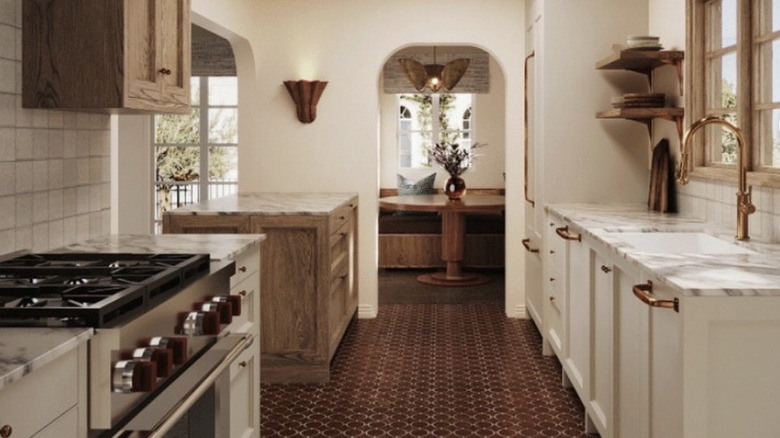A warm-toned kitchen with rusty tile floors and a kitchen nook at the far end of the kitchen through an arched doorway