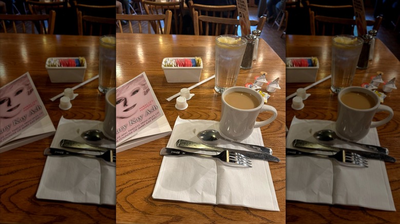 A cup of coffee next to cutlery and a book at Cracker Barrel